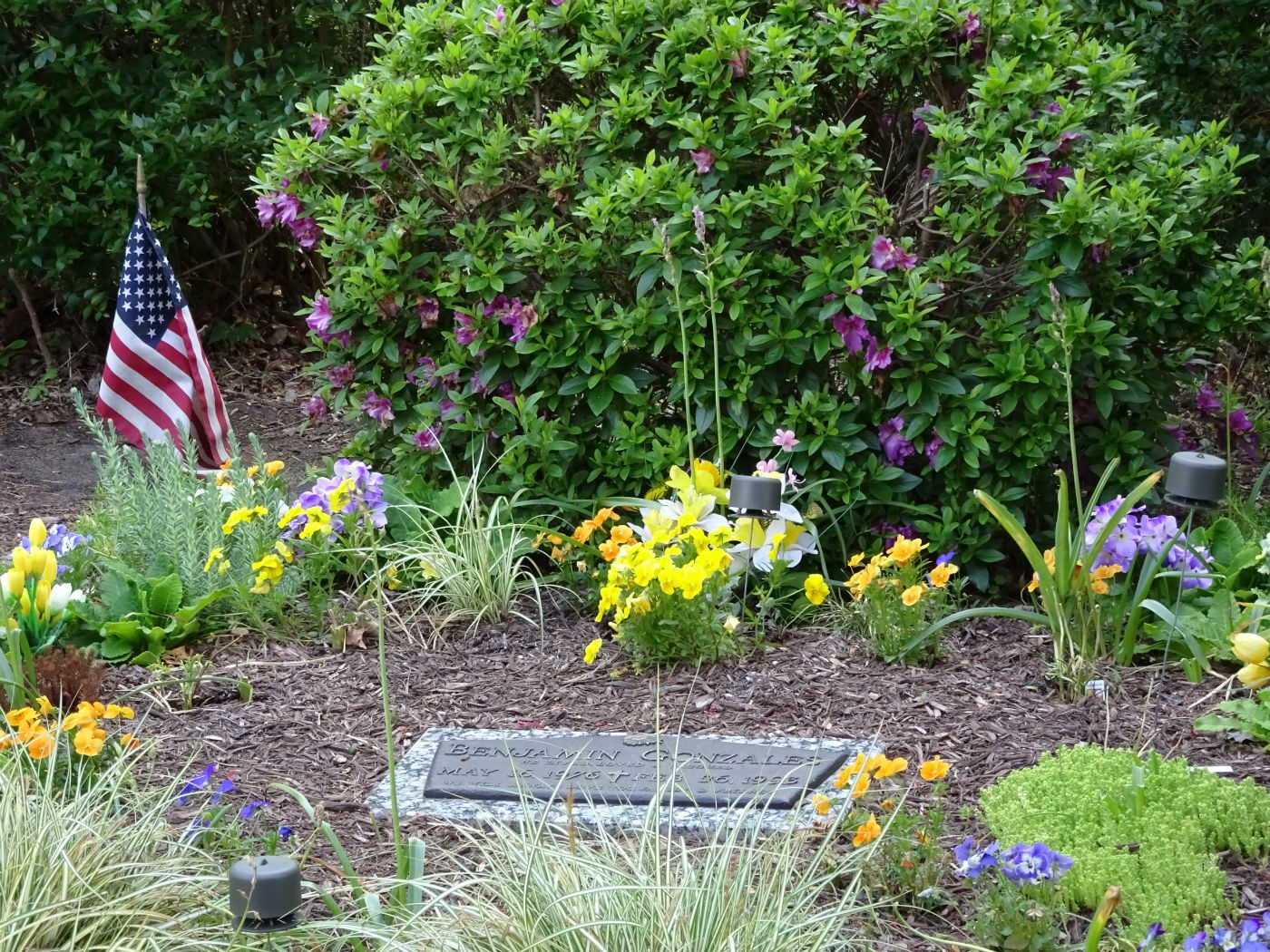 headstone surrounded by flowers and american flag
