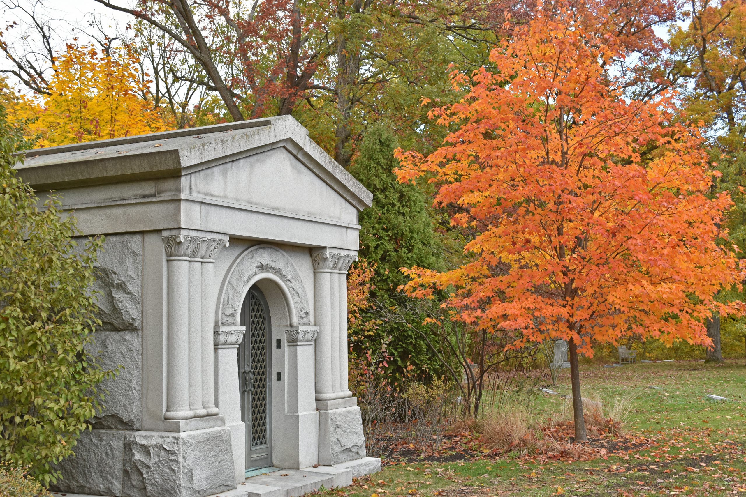 A white stone mausoleum sits amidst the orange and yellow autumn trees